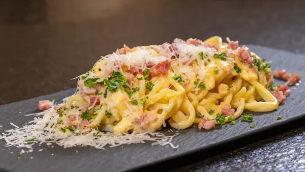 Ein Teller cremiger Spaghetti Carbonara, garniert mit Speckwürfeln, Petersilie und frisch geriebenem Parmesan.
