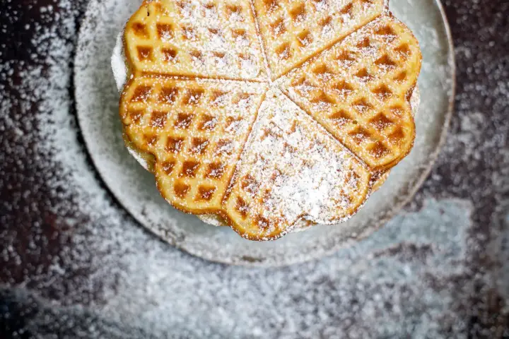 Herzförmige Waffeln, bestäubt mit Puderzucker, sehen aus wie aus einem perfekten Waffeln Rezept.