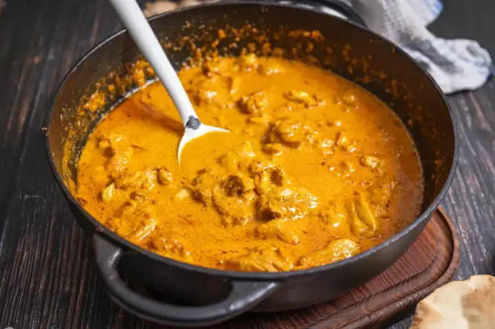 Cremiger Butter Chicken in einer Pfanne, bereit zum Servieren. Ein Löffel ragt aus der köstlichen Sauce.