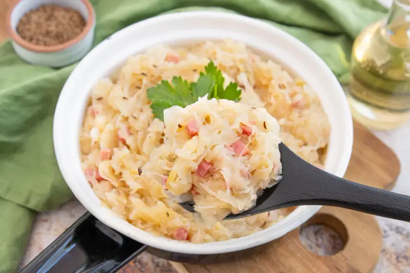 Herzhaftes Sauerkraut nach Hausfrauenart mit Speck und Kümmel, garniert mit Petersilie. Ein Löffel voller Tradition.
